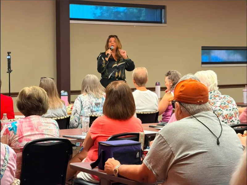 Sherri Combs speaking with a microphone in front of a seated audience of seniors at a fraud awareness workshop
